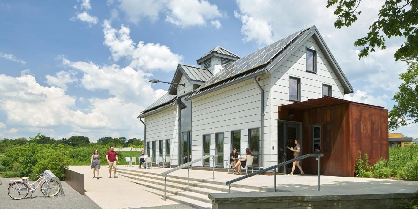 Photo of Chatham University students walking past the white dairy barn with solar panels on the roof at the Eden Hall campus.